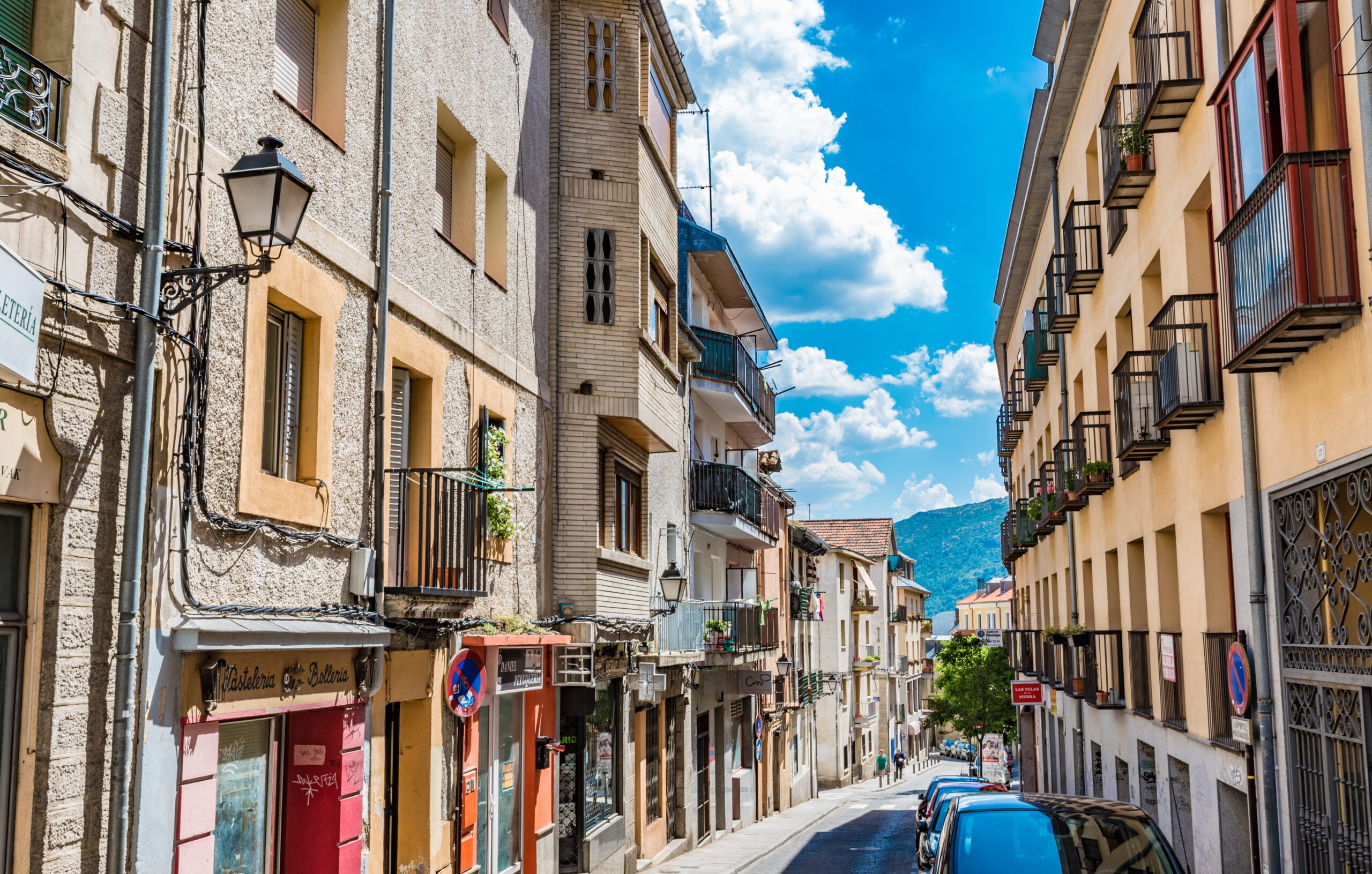 Narrow residential street in a Madrid suburb with balconies, parked cars and mountain views