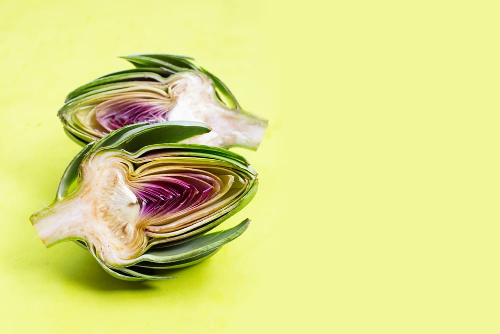 Fresh artichoke cut in half, revealing its tender heart and vibrant purple center, isolated on a green background.