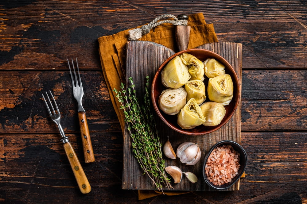 Prepared artichoke hearts with garlic, thyme and sea salt on a rustic wooden table.