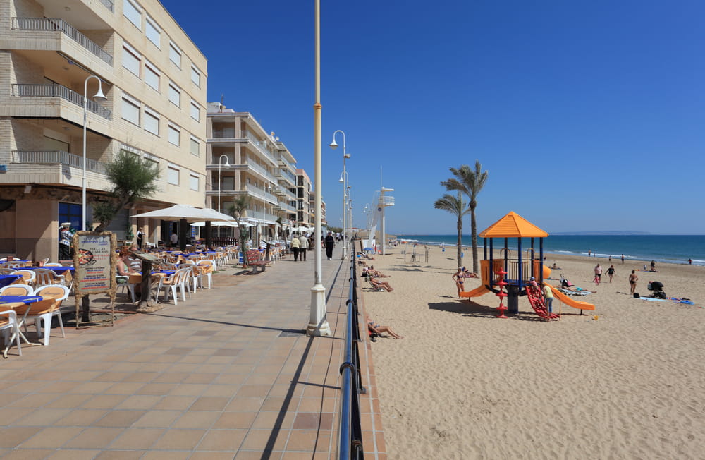 Beach promenade in Guardamar del Segura with seaside restaurants, apartment buildings, a sandy beach and children’s playground.