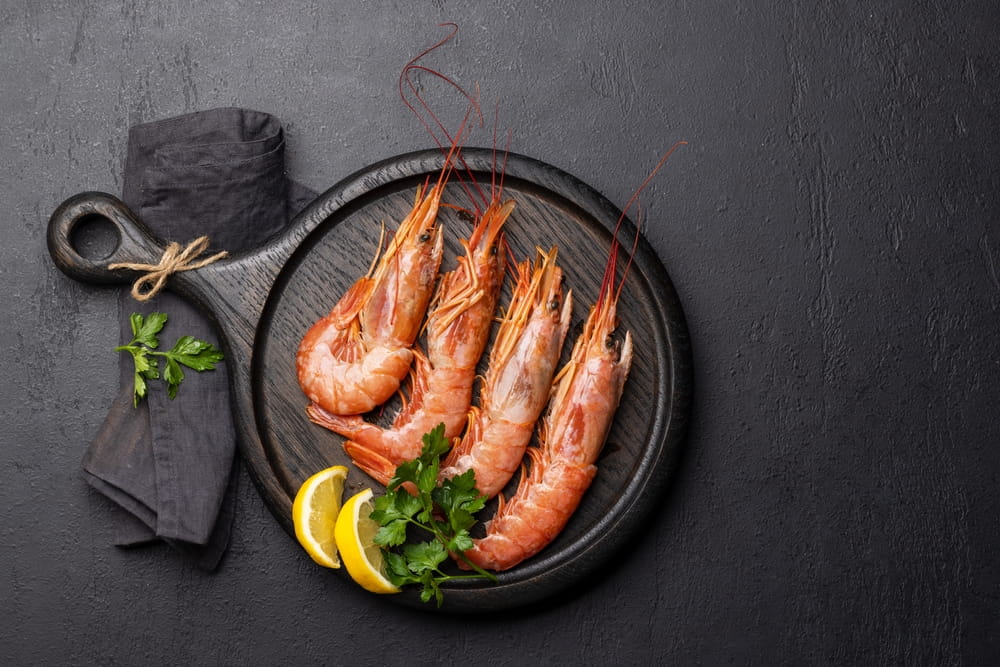 Cooked langoustines on a dark wooden board with lemon wedges, parsley and a black napkin.