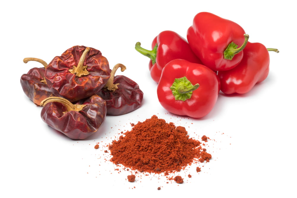 Dried ñora peppers, fresh red peppers and ground paprika on a white background.