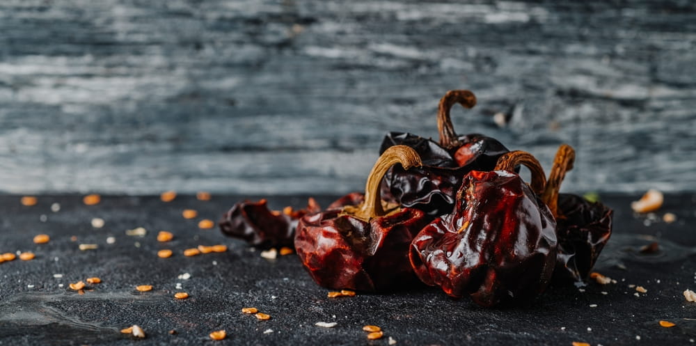 Dried ñora peppers on a dark rustic surface with scattered seeds.